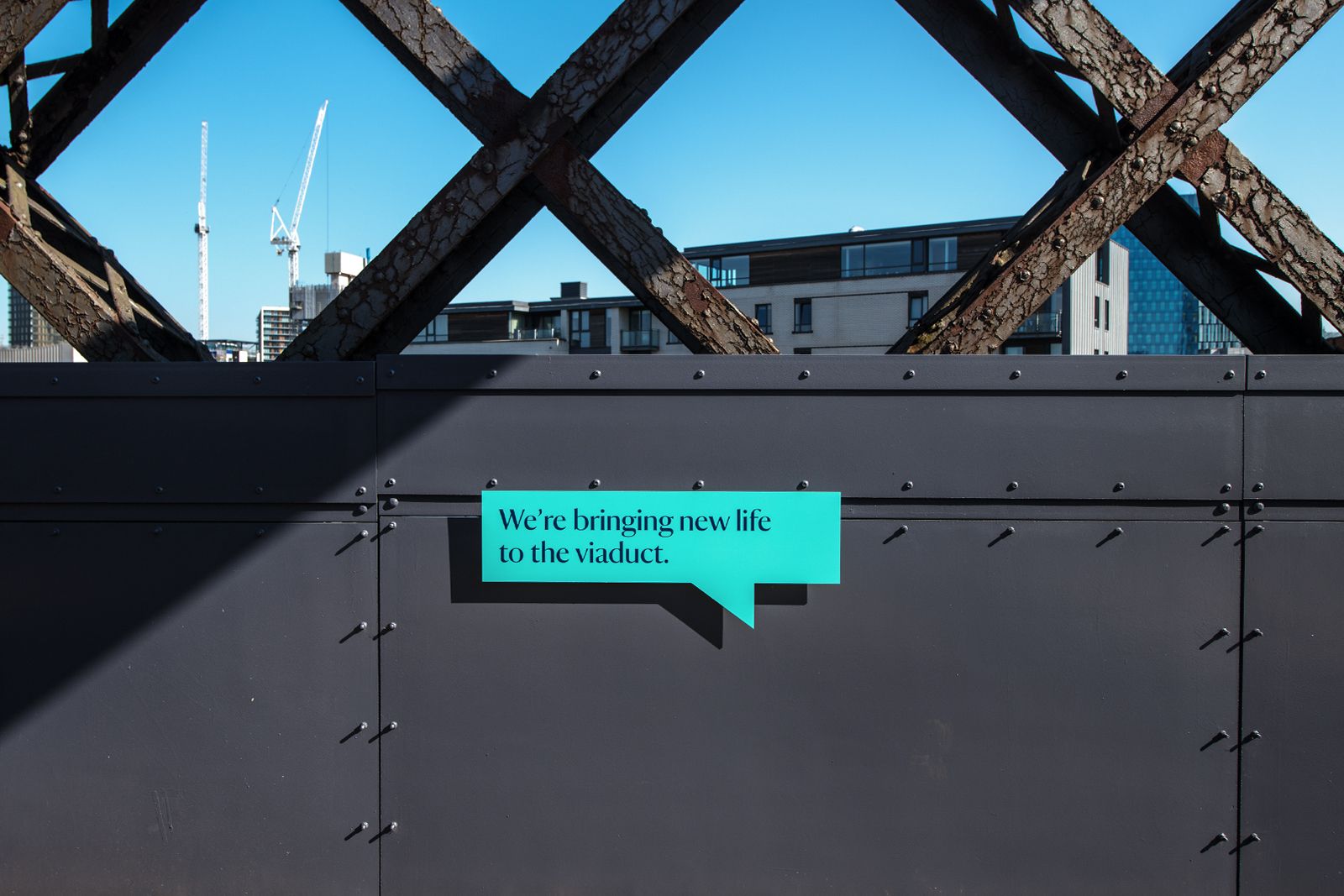 O Street Glasgow National Trust - Manchester Castlefield Viaduct branding. Teal speech bubble on industrial architecture with the text: We're bringing new life to the viaduct. Photography by Jill Jennings
